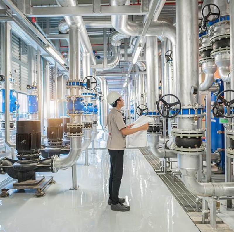 Engineer inspecting piping and reviewing technical drawings